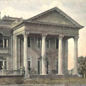 Two story stone building with covered entrances at right angles supported by immense columns