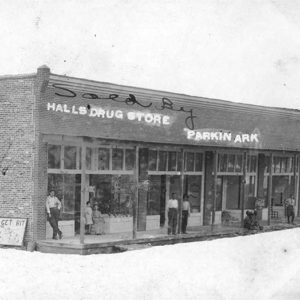 Men standing on sidewalk in front of brick building "Halls Drug Store"