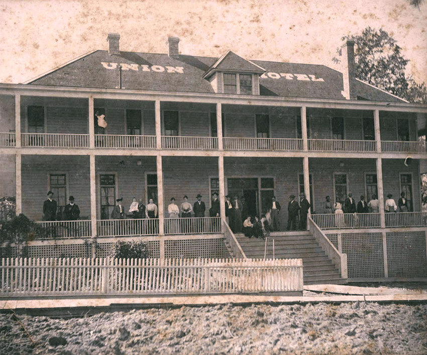 Large group of people gathered on long porch of two story building with "Union Hotel" painted on roof