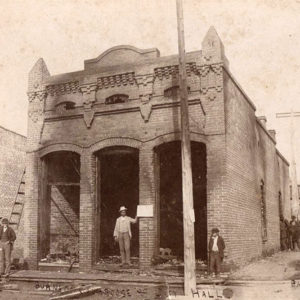 Men standing about burned out brick building
