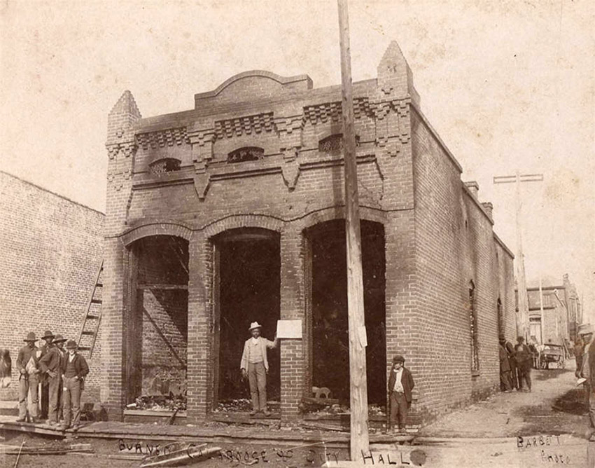 Men standing about burned out brick building