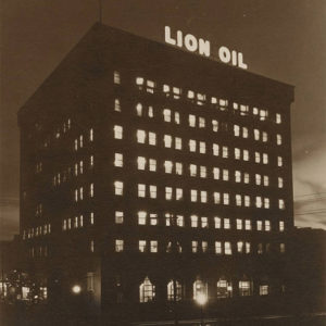 Tall multistory building at night with glowing sign "Lion Oil"