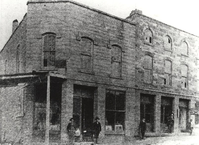 Men standing before two story stone building