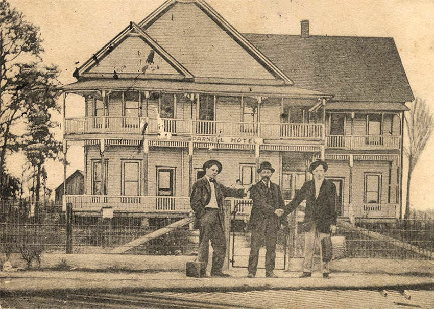 Three white men standing in front of multistory wooden house