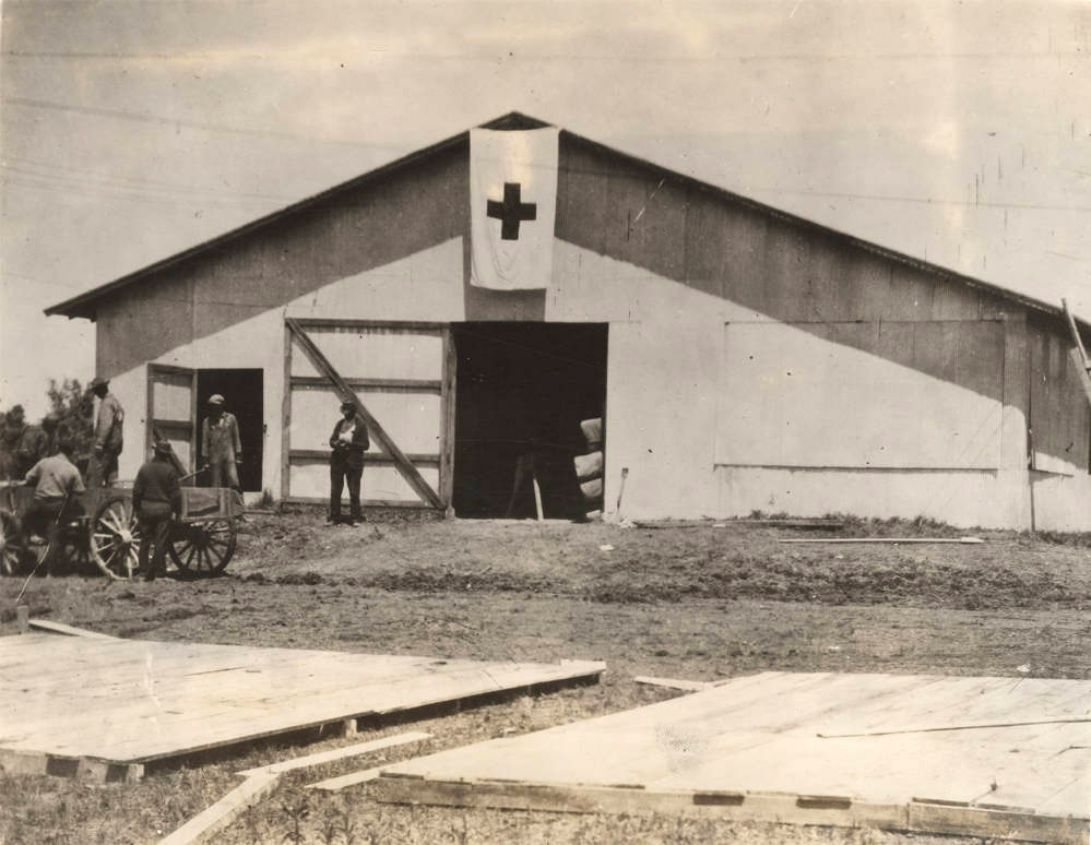 Men standing around barn-like building with large cross on it
