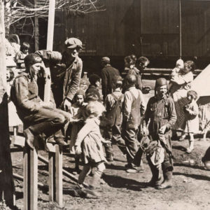 Large number of children milling about outside wooden structure