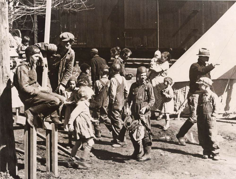 Large number of children milling about outside wooden structure