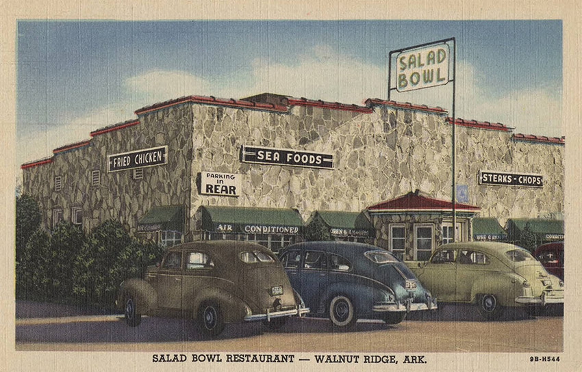 Cars parked in front of stone building with signs saying "Salad Bowl" "Steaks Chops" "Sea Foods" "Fried Chicken"