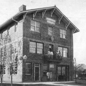 Three story brick building with people standing on second story balcony