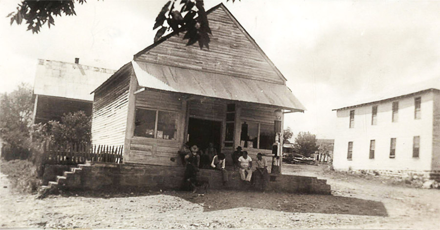 Group of men sitting on porch of wooden building with awning