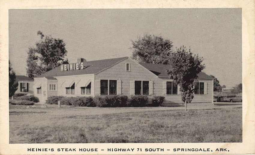 White single story building with siding and sign on roof saying "Heinie's"