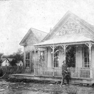 White man standing in front of wooden house with covered porch