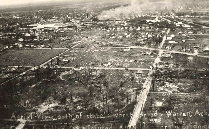 Aerial view of town with damaged buildings and smoke rising from certain places