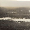 Aerial view of railroad bridge across flooded river with heavily forested land on both sides