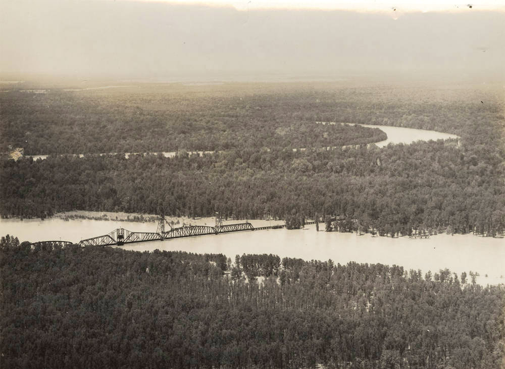 Aerial view of railroad bridge across flooded river with heavily forested land on both sides