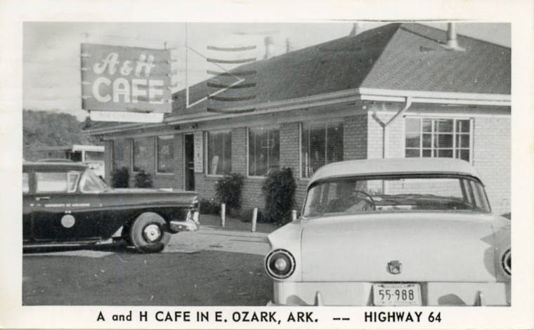 Single story white building with cars parked around it with sign saying "A and H Cafe"