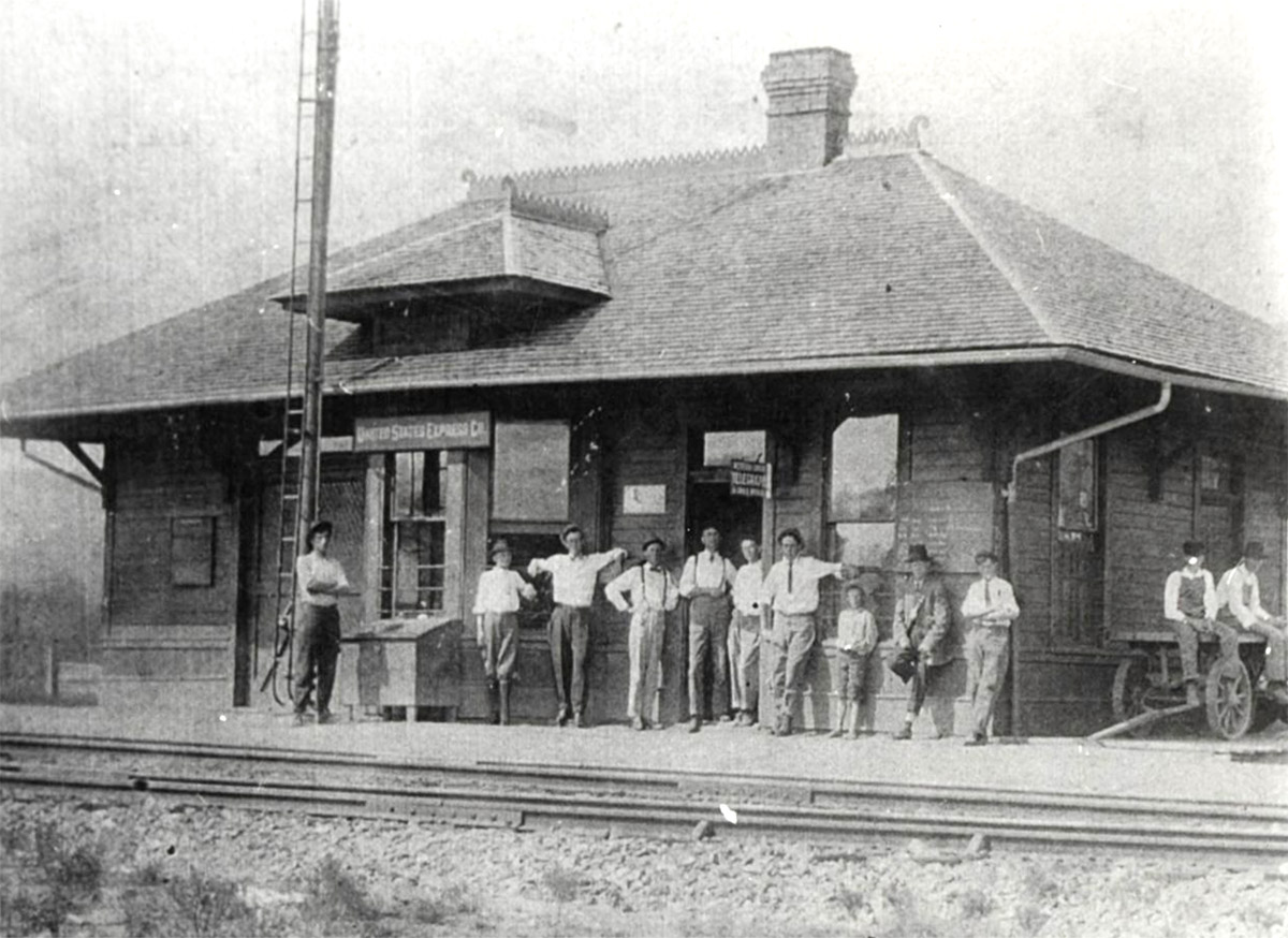 Group of people standing on porch of single story building next to railroad tracks