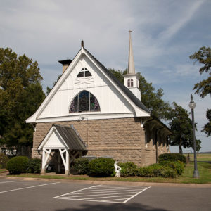 Multistory stone church with steeple and parking lot