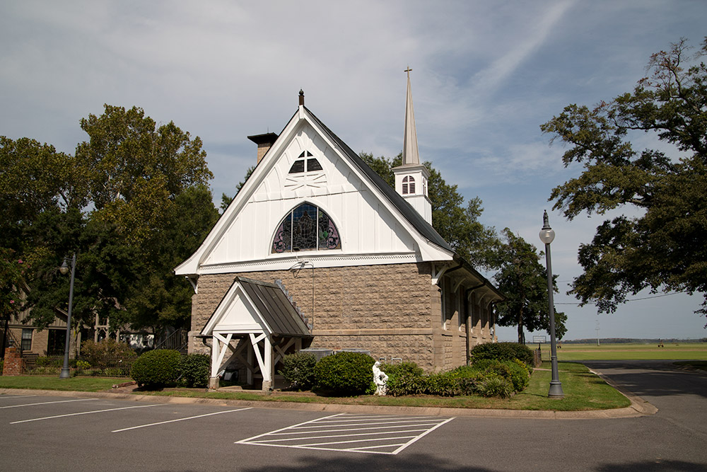 Multistory stone church with steeple and parking lot