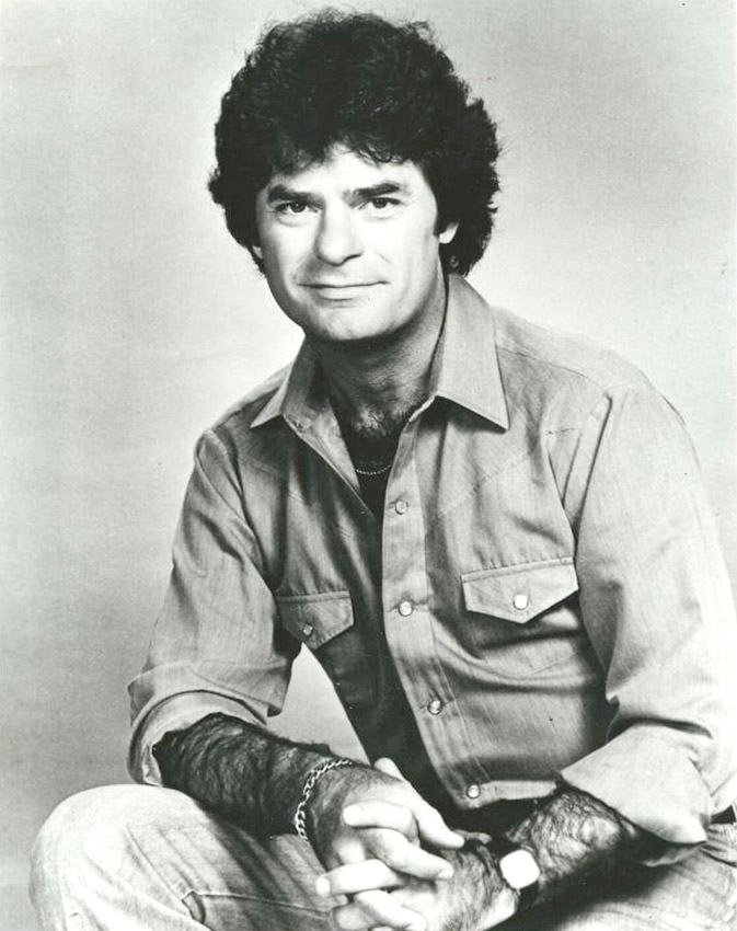 White man with dark curly hair and a button down shirt