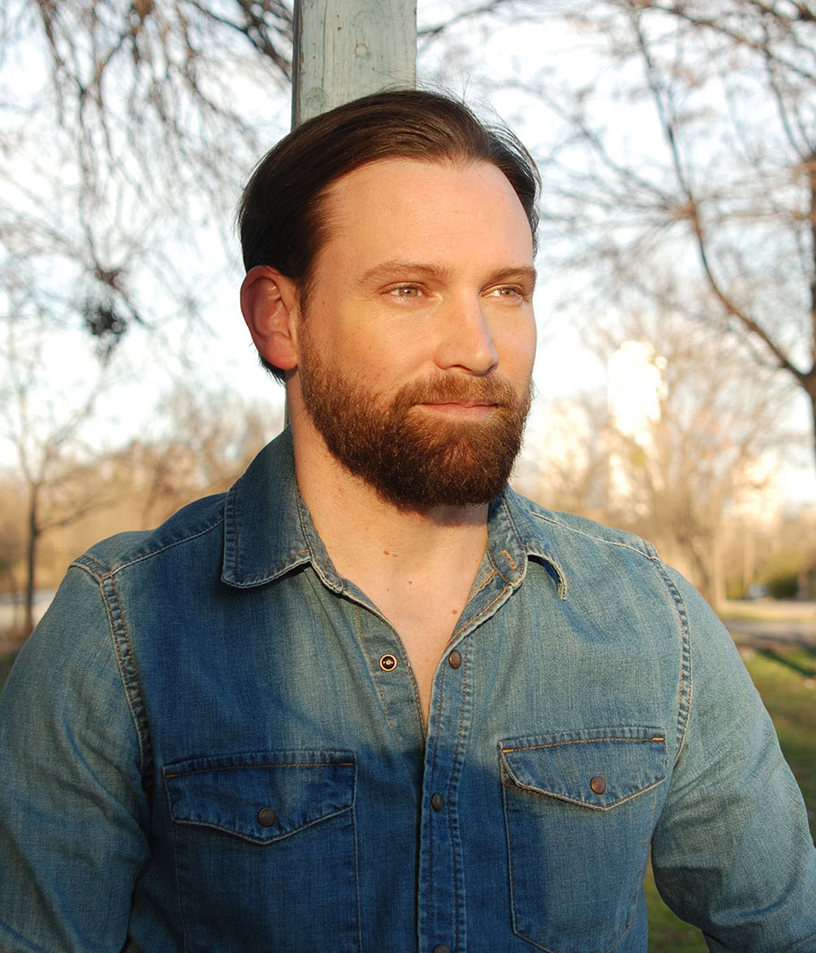 Bearded white man in denim shirt with snaps staring off into the distance