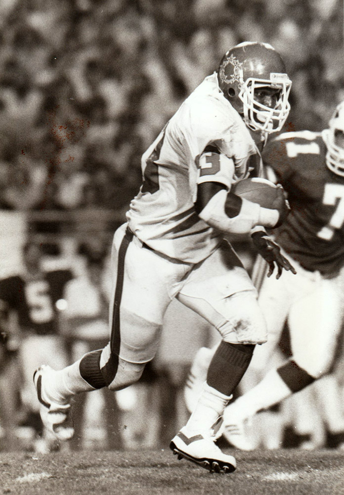 African American man in football uniform running with a football during a game