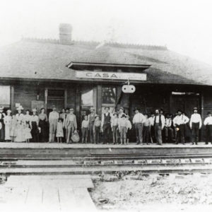 Group of people standing on porch of single story building labeled "Casa"