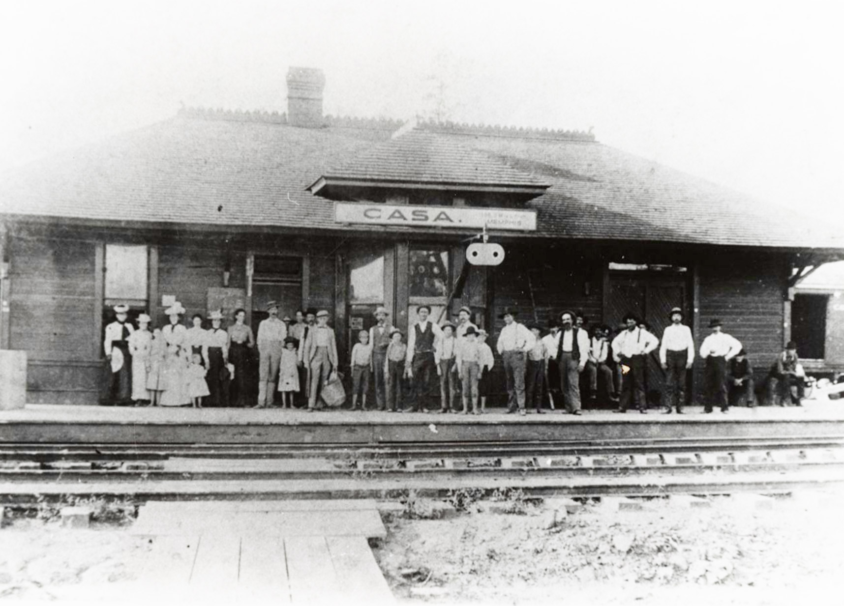 Group of people standing on porch of single story building labeled "Casa"