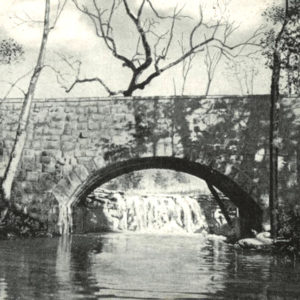 Stone bridge spanning creek with waterfall in background