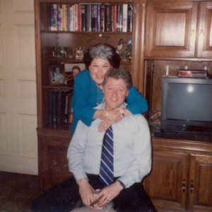 White man seated with older white woman hugging him from behind