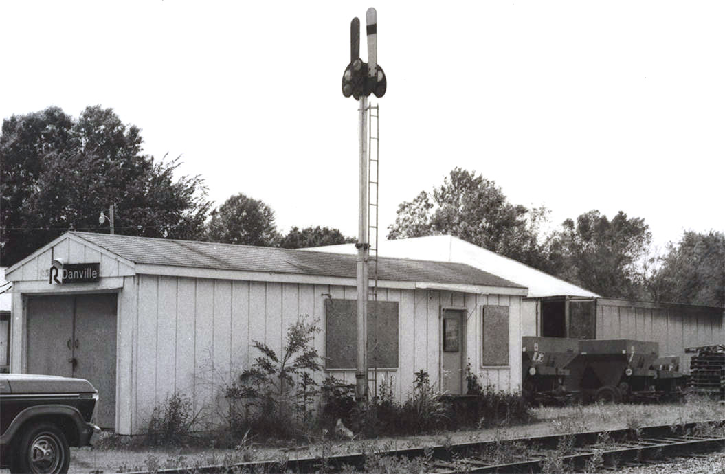 Single story white building with train signal post next to railroad line
