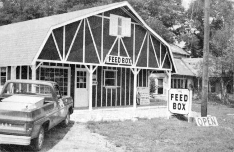 Barn-like building with pickup truck parked in front and sign saying "Feed Box"