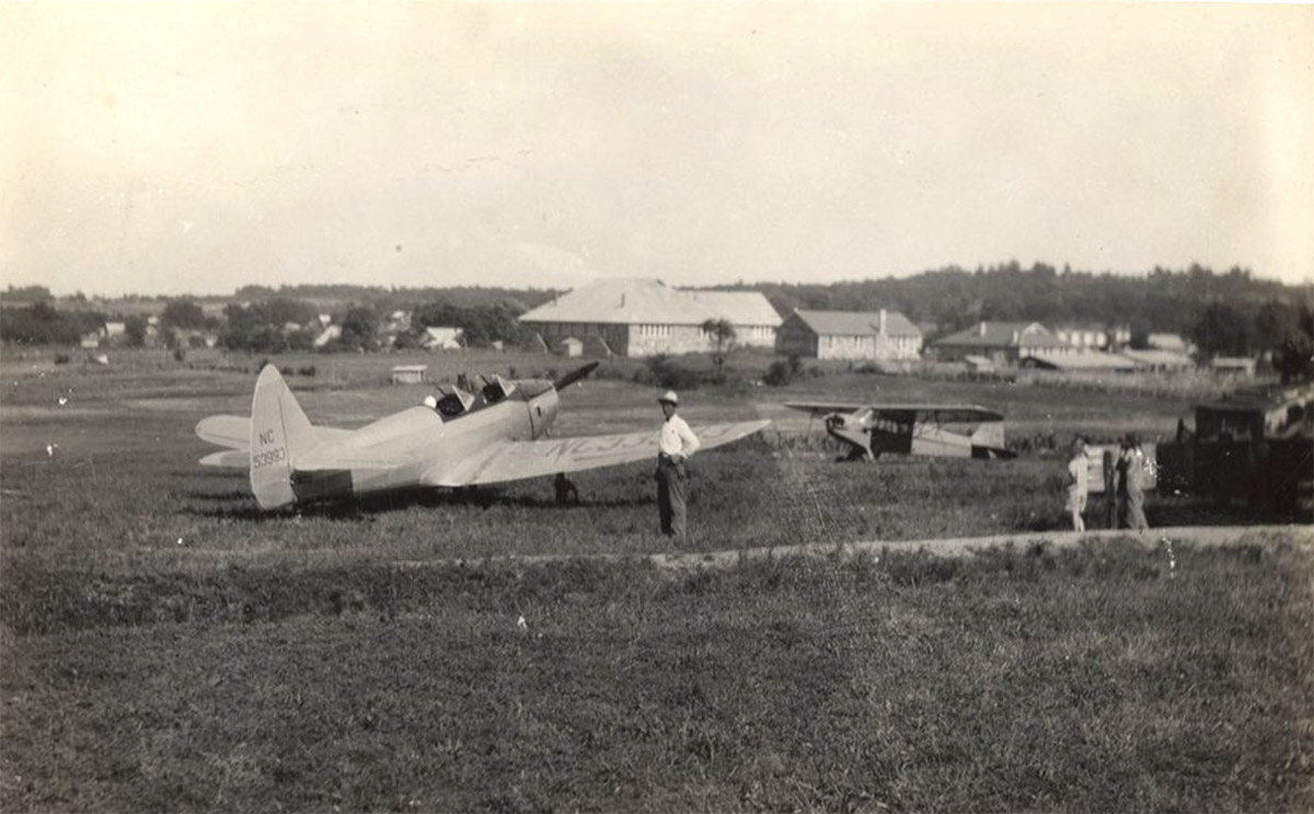 Airplanes and people in field with houses in the background