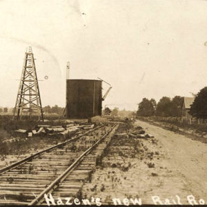 Railroad tracks running alongside metal derrick and cylindrical water tank