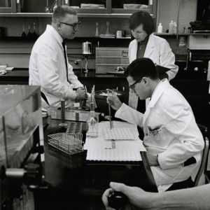 Three white people in research lab wearing white jackets