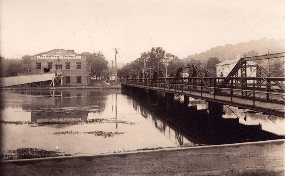 Bridge over river with multistory brick building in background by the far shore