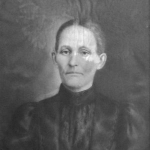 White woman with serious expression with hair pulled back and wearing a black dress