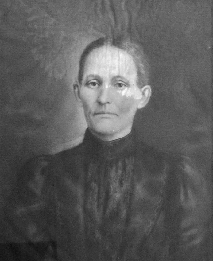 White woman with serious expression with hair pulled back and wearing a black dress