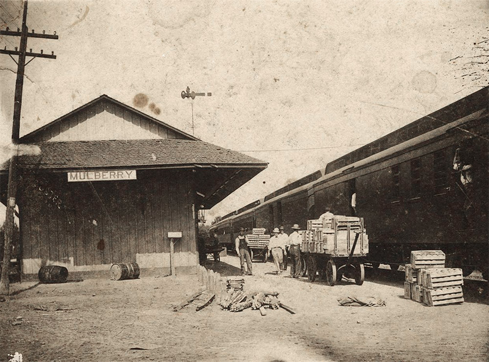 Men standing between train and single story wooden building beside railroad tracks