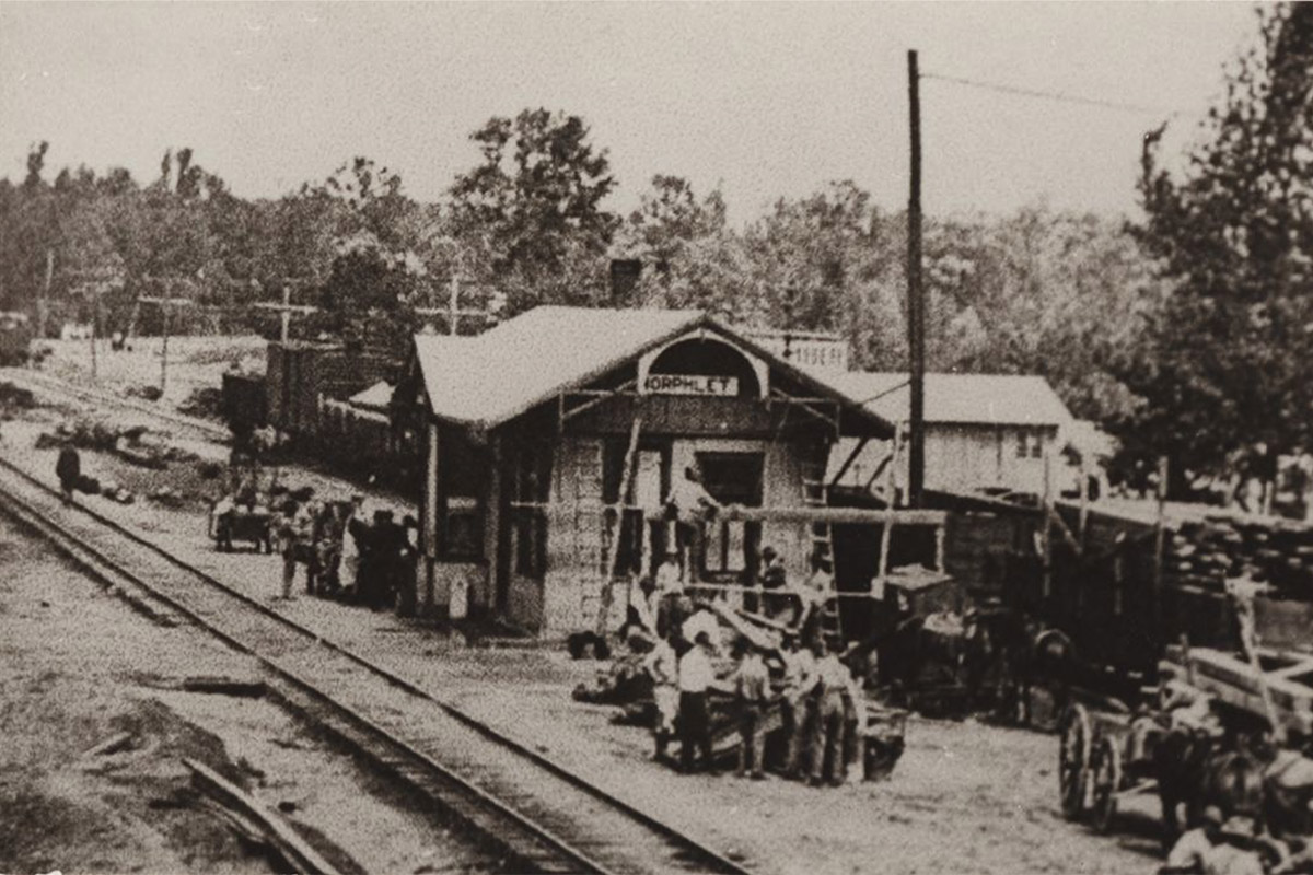 Wooden building beside railroad tracks with people and machinery around