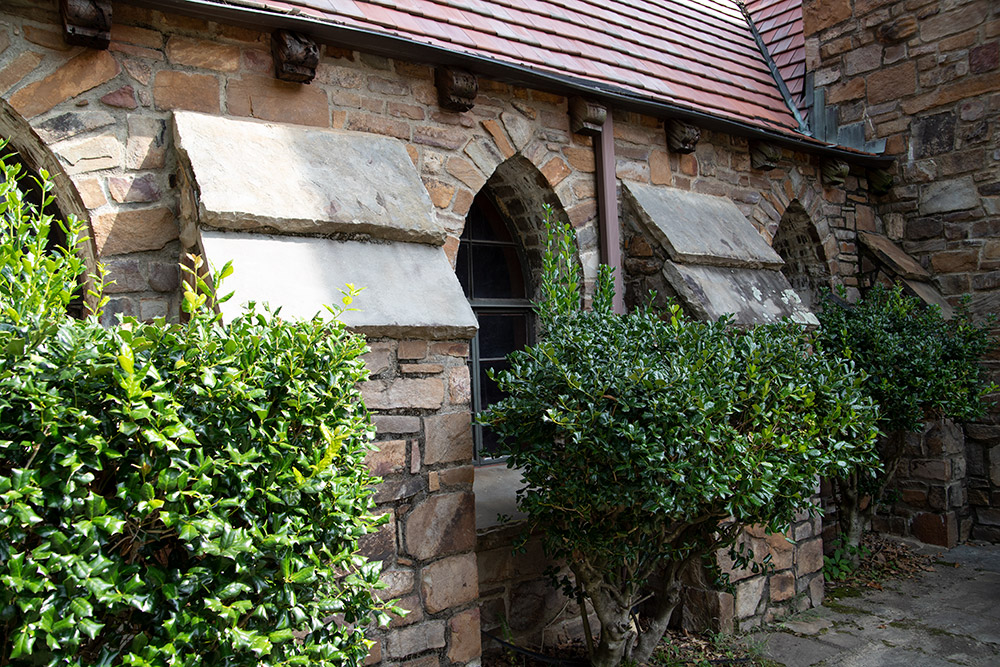 View of windows in stone building with red roof and exterior bushes