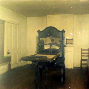 Room with white walls and several pieces of furniture and old-fashioned printing press