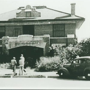 Multistory building with porch and people and cars in front