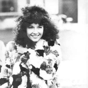 White woman with curly dark hair smiling in rabbit fur coat