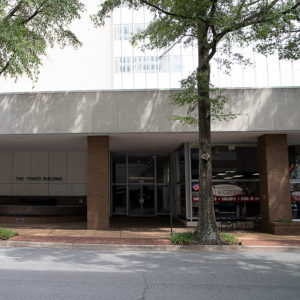 Urban ground-level storefront with exterior trees and "The Tower Building" displayed on the wall