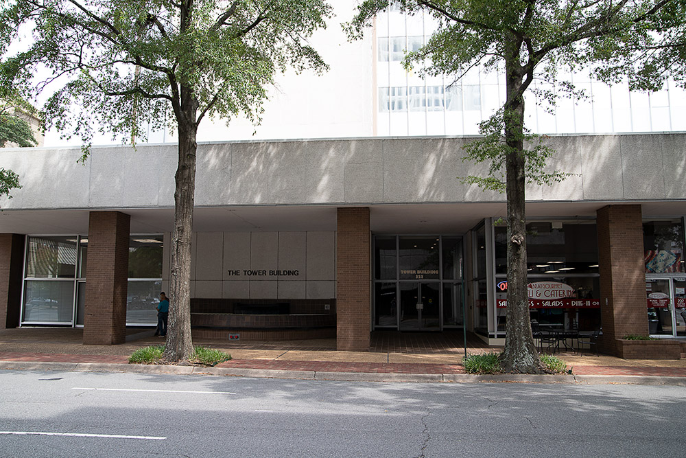 Urban ground-level storefront with exterior trees and "The Tower Building" displayed on the wall