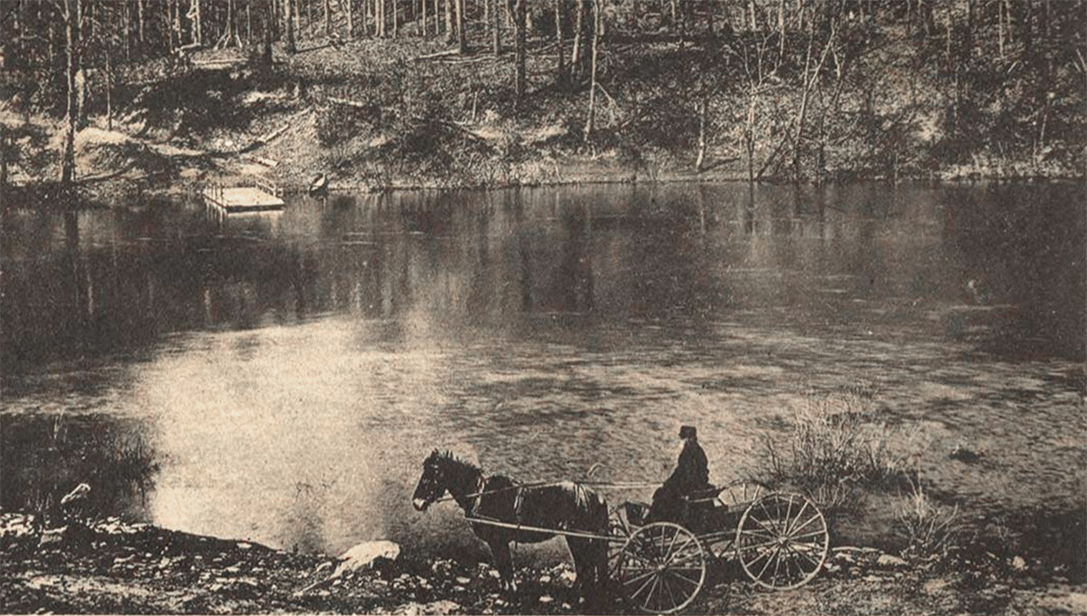 Horse and buggy and driver beside river with landing dock in background