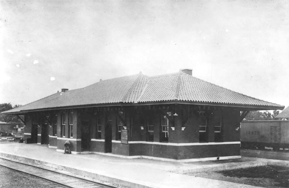Single story brick building beside railroad tracks with train alongside