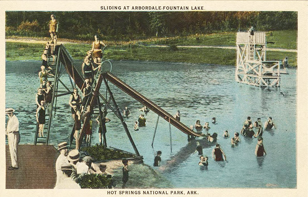 Adults and children in swimming gear at lakeside with two metal slides in foreground