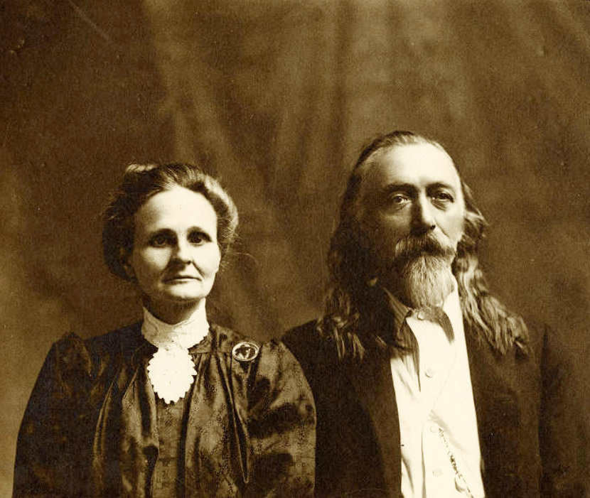 Older white man with long hair and beard beside woman with pulled-back hair in dress